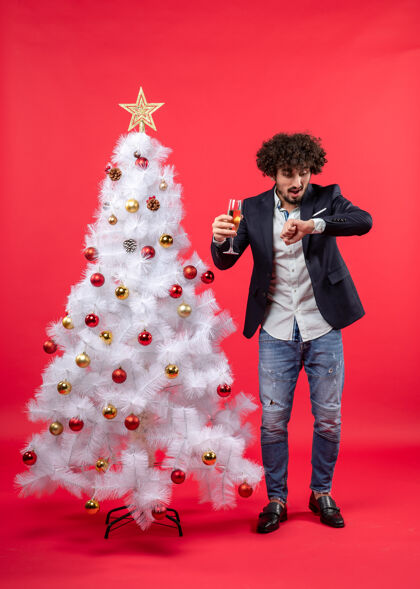 可爱圣诞节庆祝活动与留胡子的年轻人与葡萄酒检查时间 站在圣诞树附近的红色年轻男人站着