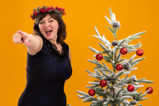 印象深刻令人印象深刻的中年妇女头戴圣诞花环 脖子上戴着金箔花环 站在装饰过的圣诞树旁女人金属片树