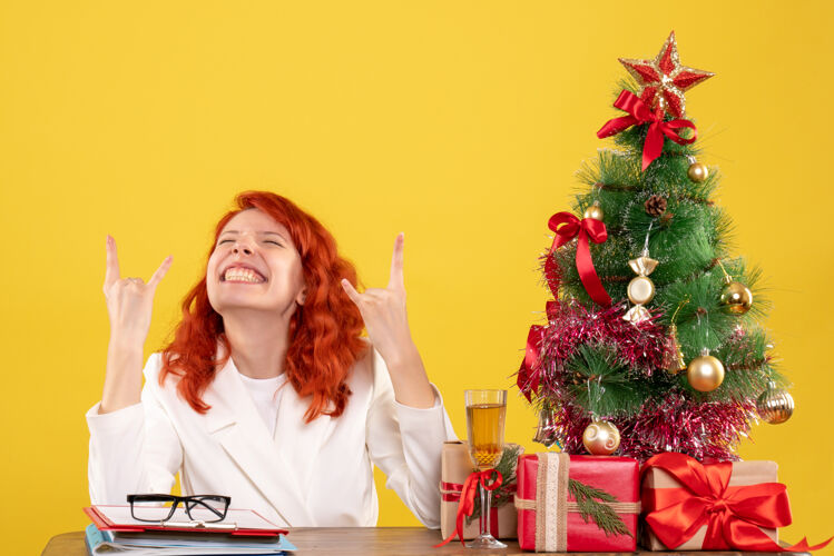 桌子正面图：女医生坐在桌子后面 黄色桌子上放着圣诞礼物和圣诞树女性桌子微笑