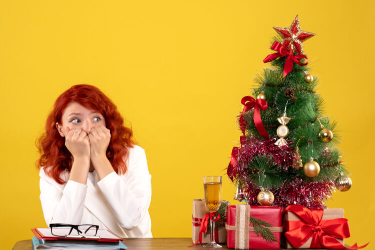 办公室女工人坐在桌子后面 手里拿着圣诞礼物和黄色的圣诞树女工人礼物桌子