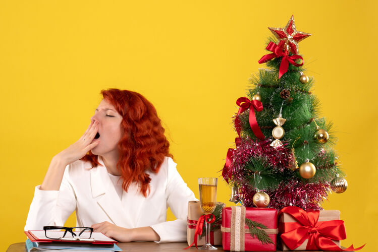 女女工人坐在桌子后面 手里拿着圣诞礼物和黄色的圣诞树坐着女工人情感