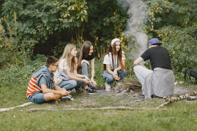 冒险探险 旅游 远足和人的概念一群微笑的朋友在森林里人们坐在篝火旁森林生态朋友