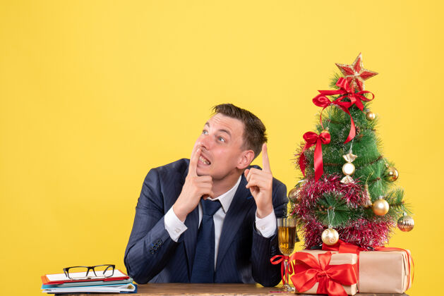 思考前视图思考的人坐在圣诞树附近的桌子和黄色的礼物商人圣诞节礼物