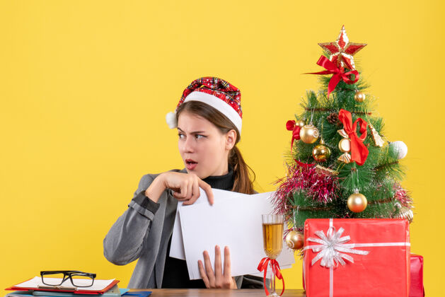帽子正面图：戴着圣诞帽的女孩坐在桌旁 手里拿着圣诞树和礼物鸡尾酒生活好奇的女孩礼物