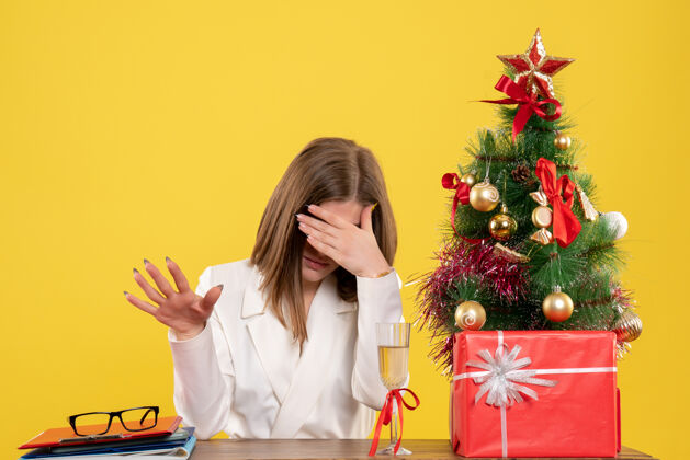 花正面图：女医生坐在桌子前 黄色背景下 圣诞树和礼盒显得格外显眼圣诞节人女医生