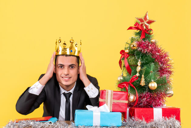 微笑前视图微笑着戴着皇冠的男人坐在桌旁圣诞树和礼物礼物礼物男人