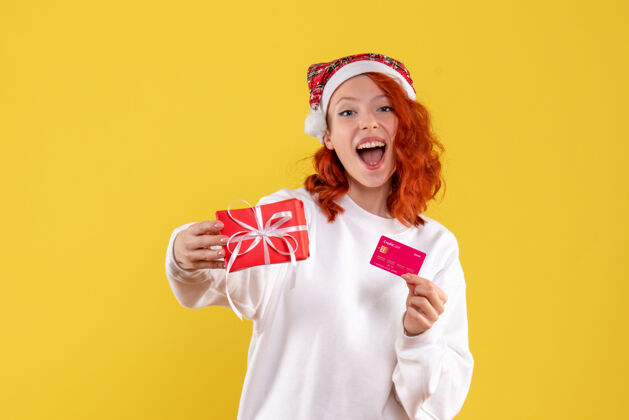 礼物圣诞礼物和黄墙上银行卡的年轻女子的正面图情感人微笑