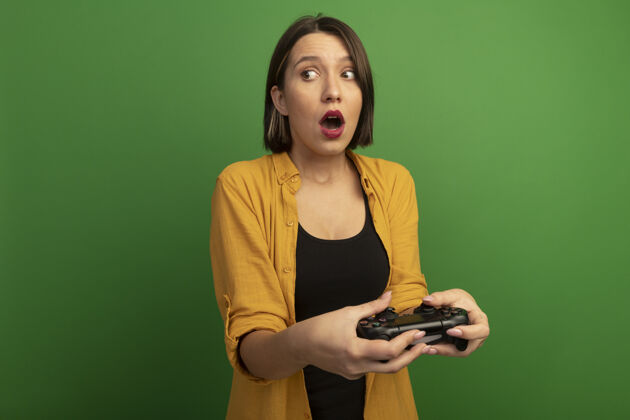 玩家惊艳美丽的白种女人拿着游戏控制器 看着一旁的孤立无援绿色控制器漂亮