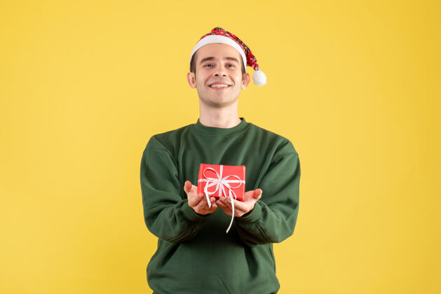 圣诞节正面图微笑的年轻人拿着圣诞礼物站在黄色的椅子上英俊空间站立