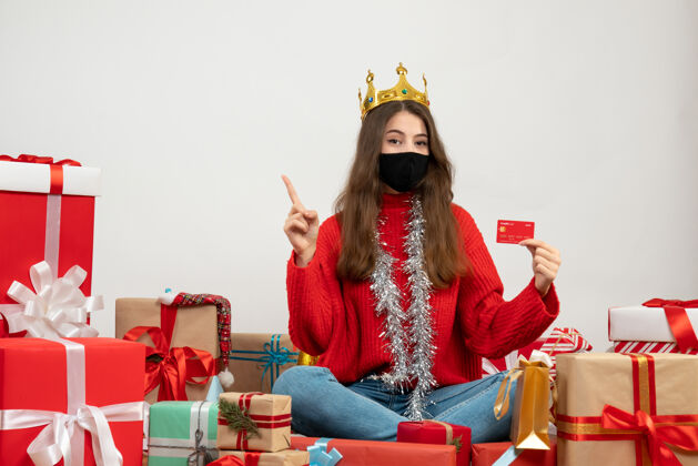 肖像穿着红色毛衣拿着卡片的圣诞女孩围坐在礼物旁边 白色的面具是黑色的文化女孩毛衣