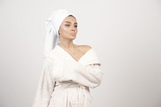 人穿着白色浴袍的漂亮年轻女子在白墙上摆姿势头毛巾治疗