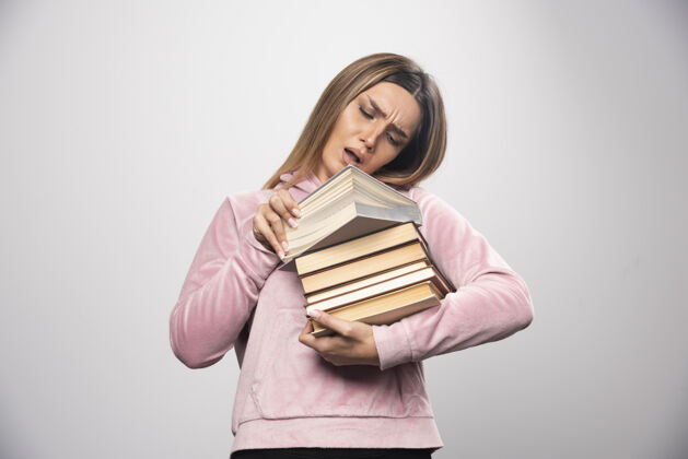 成人穿着粉色运动衫的女孩手里拿着一堆书 打开上面的一本读着学习年轻粉色