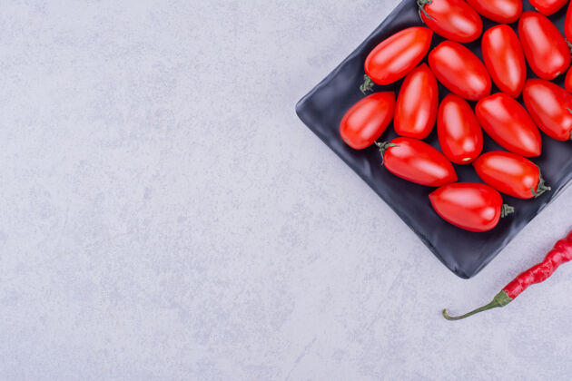 产品樱桃番茄和红辣椒放在一个黑盘子里生物清淡辣椒粉