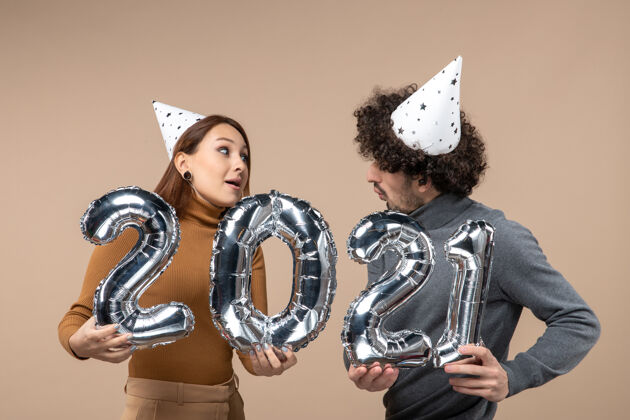 姿势幸福的年轻夫妇互相看着戴着新年帽的姿势 镜头里的女孩和穿灰色衣服的男人成年人年轻人小伙子