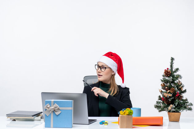 商务戴着圣诞老人帽的金发女人坐在桌子旁 手里拿着圣诞树和礼物圣诞老人女人笔记本电脑