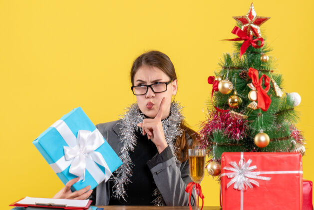 礼物前视图体贴的女孩戴着眼镜坐在桌边放手指圣诞节花束树