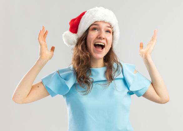顶穿着蓝色上衣 戴着圣诞帽的年轻女子高举双臂尖叫着疯狂的快乐和兴奋年轻快乐新