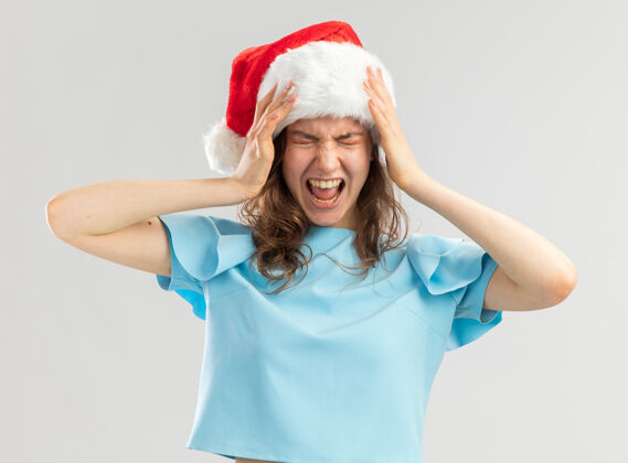 帽子穿蓝上衣戴圣诞帽的年轻女子手举着头 带着恼怒的表情大喊大叫头女人圣诞