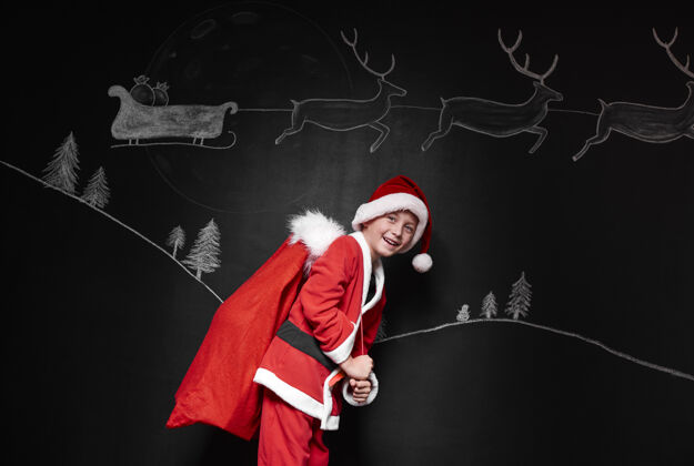 男孩一个穿着圣诞老人服装的男孩背着一袋礼物微笑站立衣服