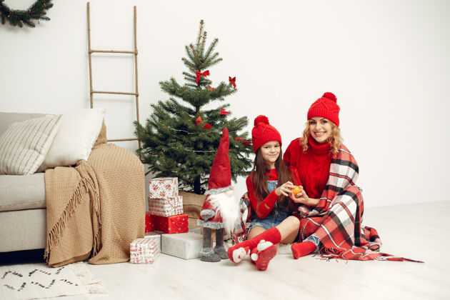 坐人们在为圣诞节做准备母亲在和女儿玩耍一家人在节日的房间里休息孩子穿着红色毛衣赠送人闪亮