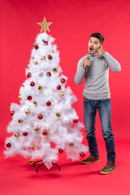 站立新年气氛积极的家伙穿着牛仔裤站在装饰圣诞树附近圣诞树心情手势