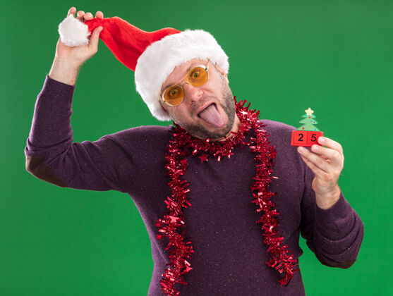 玩具顽皮的中年男子戴着圣诞帽 脖子上戴着金属丝花环 戴着眼镜 手里拿着圣诞树玩具和日期男人圣诞树眼镜