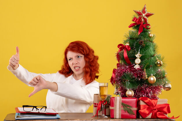 桌子女工人坐在桌子后面 拿着圣诞树和黄色的礼物树办公室坐着