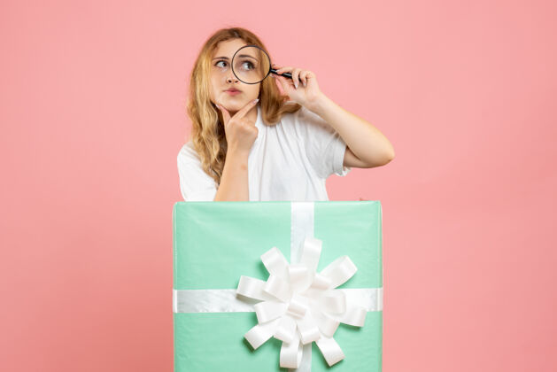 粉色前视图年轻女性在蓝色礼品盒内使用放大镜漂亮放大镜礼物