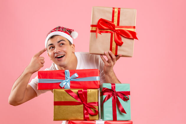 年轻男性年轻人围着粉色墙上不同圣诞礼物的前视图快乐礼品盒丝带