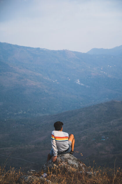 人一个人坐在岩石上沉思大自然的后视图后面山白天
