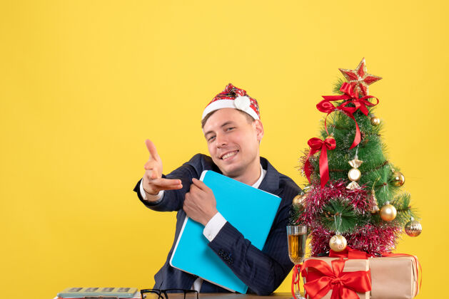 树正面图是一位快乐的商人坐在圣诞树旁的桌子旁 手把手放在黄色的礼物上生活人生意