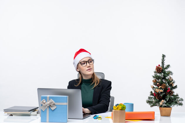 圣诞老人戴着圣诞老人帽的女商人坐在桌子旁 桌上放着圣诞树和礼物某人工作桌子