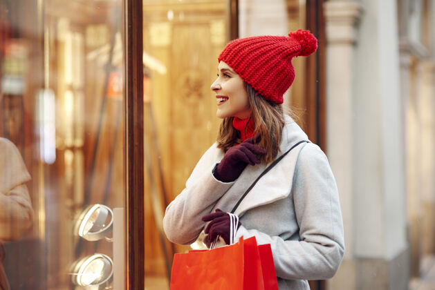 优雅美丽的女人在冬季购物时看着橱窗城市透过窗户看户外