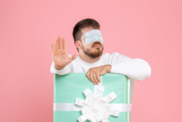 情感粉红色墙上戴着面具的年轻人在礼物盒里的正视图眼睛圣诞节微笑