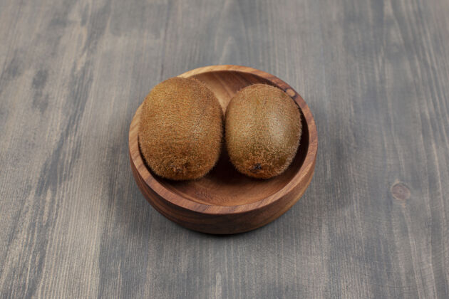 新鲜木桌上放着一个木碗和两个新鲜的猕猴桃高质量的照片好吃成熟木头