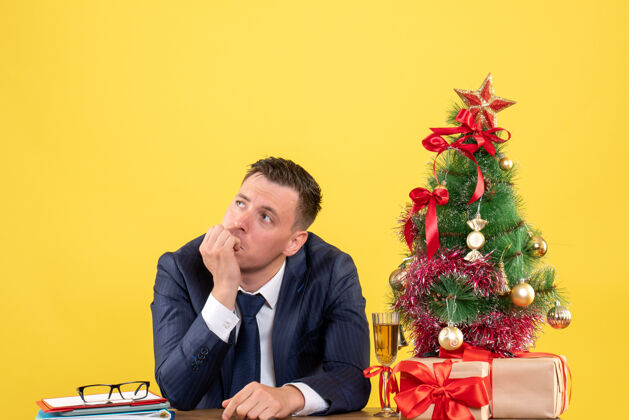 男人体贴的男人坐在圣诞树旁边的桌子上思考着什么 黄色的礼物体贴的男人有事新郎
