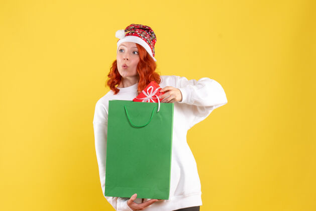 人黄色墙上拿着包裹和小礼物的年轻女子的正视图快乐年轻的女性圣诞节