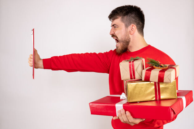 圣诞节身穿红衫的年轻人拿着圣诞礼物和白墙上的文件说明的正面视图笔记男性文件