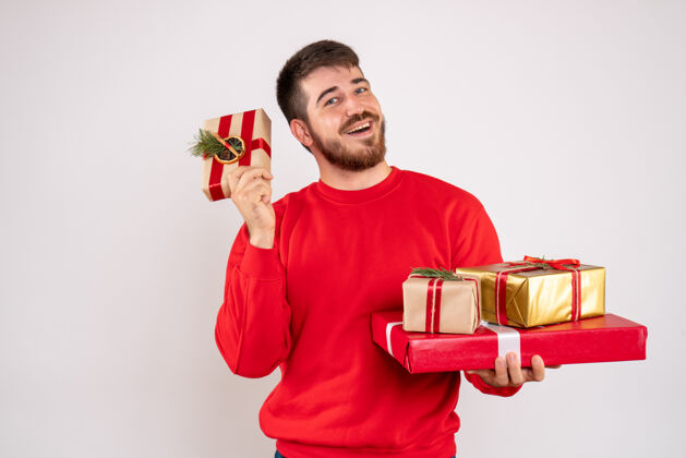 快乐身穿红衫的年轻人拿着圣诞礼物站在白墙上的正视图微笑礼物圣诞节