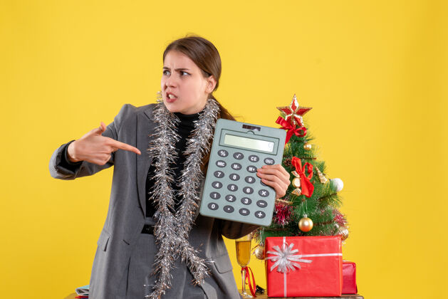 乐器前视图好奇的女孩显示计算器站在圣诞树和礼物鸡尾酒附近树乐器展示
