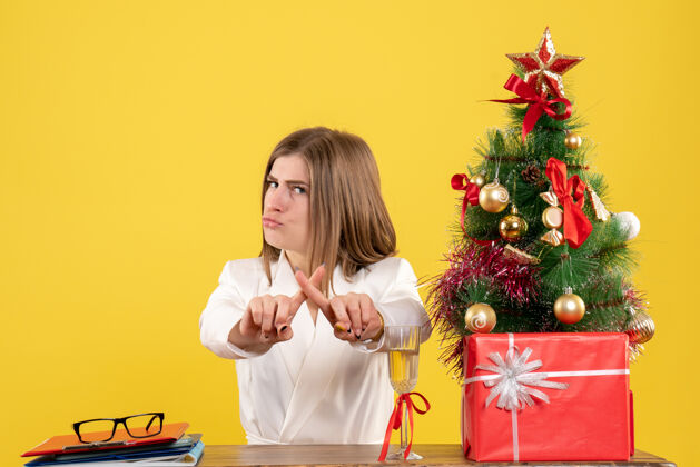 前面正面图：女医生坐在黄色背景的桌子前 放着圣诞树和礼品盒女医生人背景