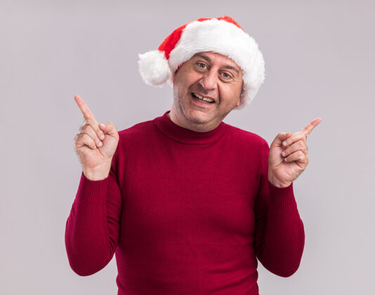 微笑快乐快乐的中年男子戴着圣诞老人帽微笑着用食指指着站在白色背景上手指站着年龄