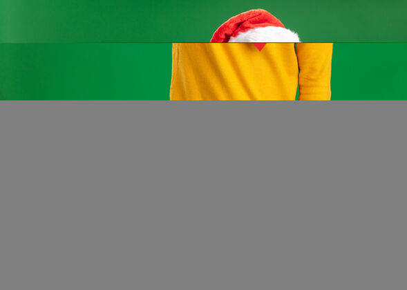 年轻人一个穿着黄色高领毛衣 戴着圣诞帽 打着滑稽领带的年轻人 带着恼怒的表情 用食指指着绿色墙壁上站着的东西大叫圣诞节指着男人