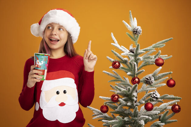 年小女孩穿着圣诞毛衣 戴着圣诞帽 手里拿着五颜六色的纸杯圣诞纸新年
