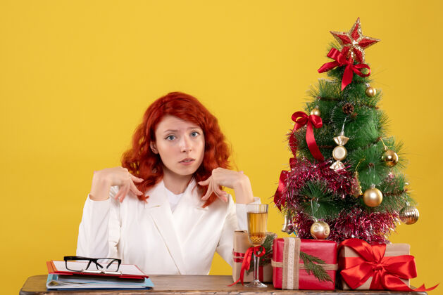 桌子女工人坐在桌子后面 拿着圣诞树和黄色的礼物办公室黄色女