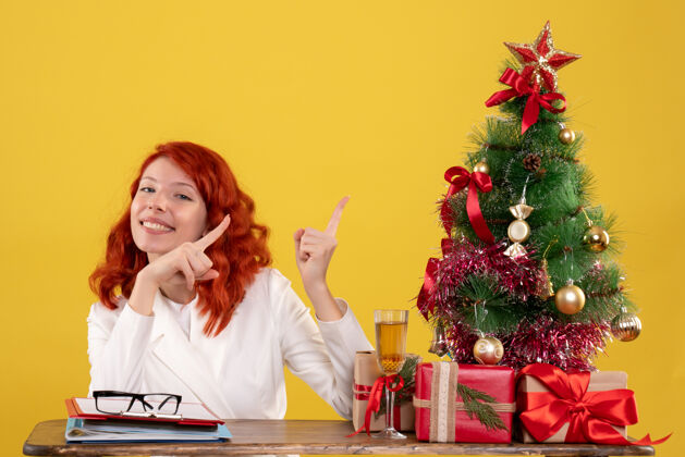 女工人女工人坐在桌子后面 拿着圣诞树和黄色的礼物女办公室礼物