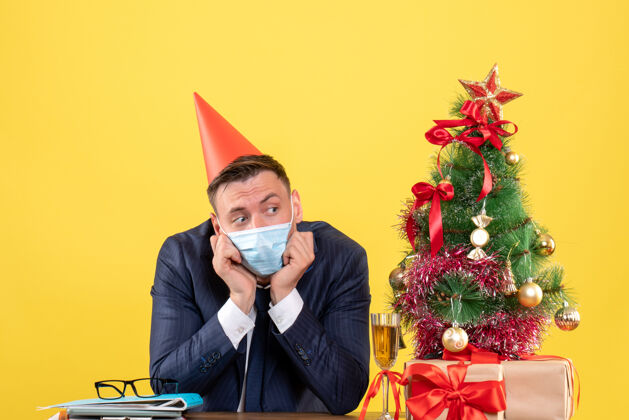 聚会前视图沮丧的商人与党帽坐在桌旁圣诞树和黄色的礼物桌子人礼物