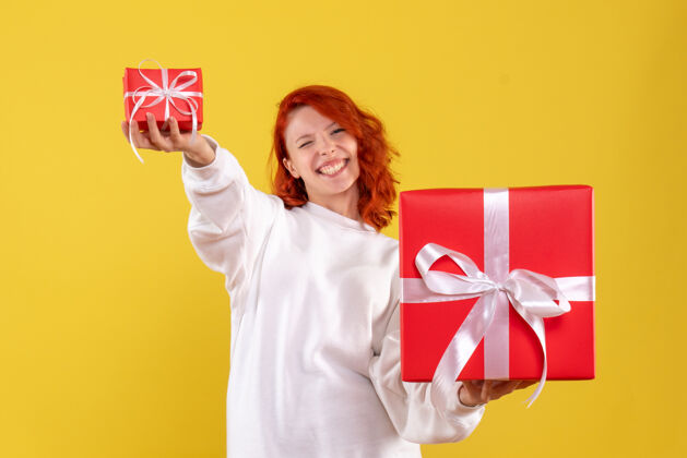 漂亮黄色墙壁上年轻女子拿着圣诞礼物的正面图人圣诞节丝带