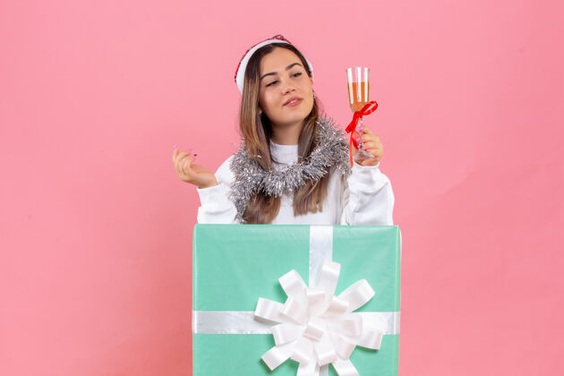 礼物前视图的年轻女子庆祝圣诞节与饮料上粉红色的墙壁年轻女性礼物