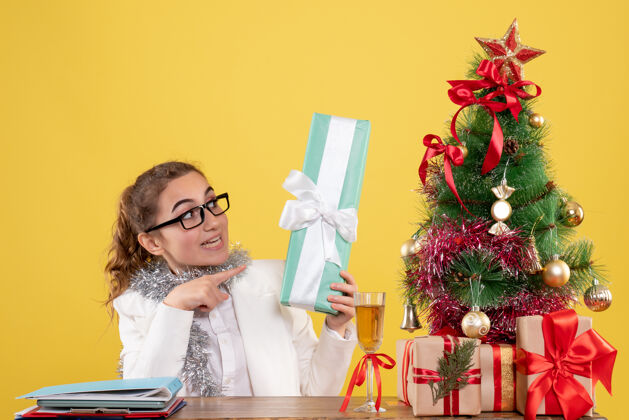 医生正面图女医生围坐在圣诞礼物和黄色背景上拿着礼物的树上鲜花背景办公室